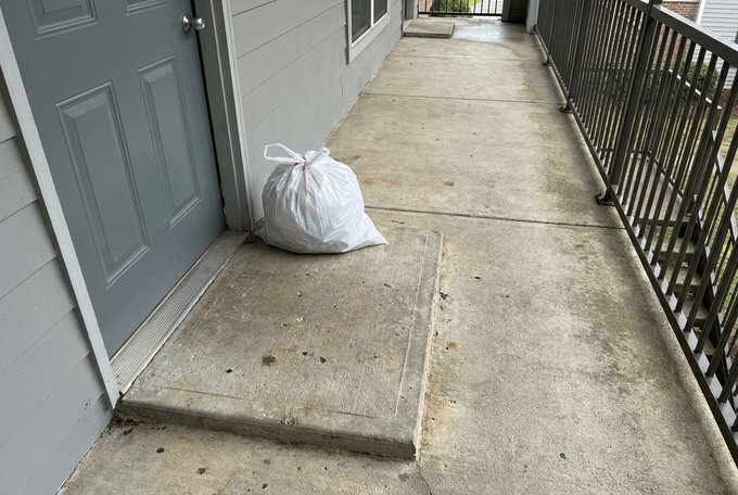 Tied household trash bag set outside an apartment door in a breezeway for doorstep valet trash collection